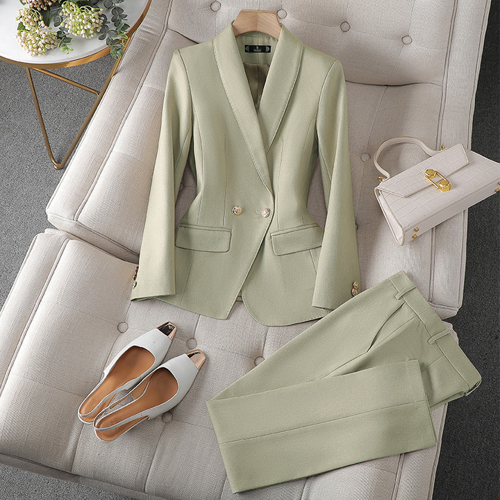 Ein hellgrüner Blazer und eine passende Hose, ordentlich auf einer weichen Oberfläche angeordnet, neben einer weißen Handtasche und stylischen Sandalen.