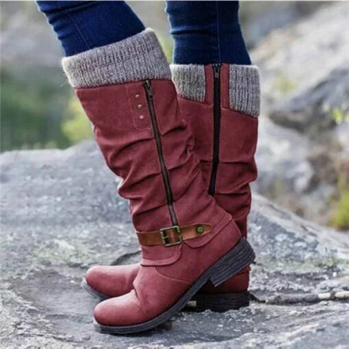 Eine Nahaufnahme eines roten orthopädischen Stiefels mit lässigem Design und Strickbund, der von einer Person getragen wird, die auf felsigem Boden steht. Das Bild hebt sein stilvolles Aussehen und seine Komfortmerkmale hervor.