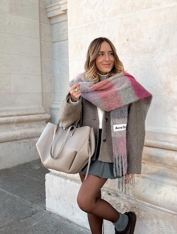 Eine frau in einem grauen mantel und buntem schal posiert mit einer taupe ledertasche